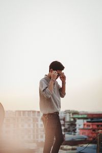 Young man standing in city against clear sky at sunset