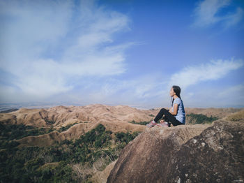 Full length of man sitting on rock against sky