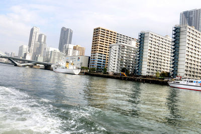 View of city at waterfront against cloudy sky