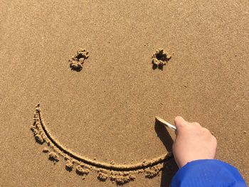 Cropped hand making smiley face on sand at beach