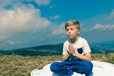 Boy sitting on mountain against sky