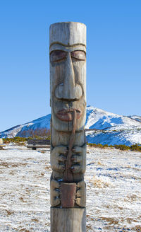 Wooden post on snow covered land against sky