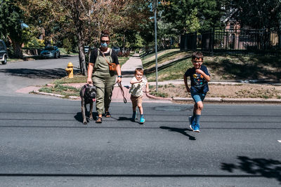 Mother and two boys running across a neighborhood street on sunny day