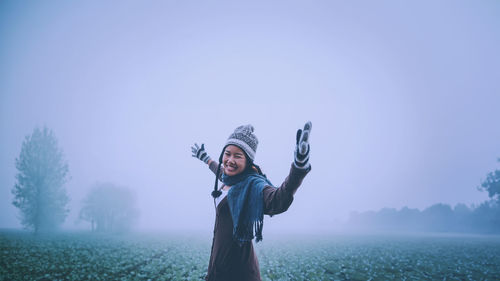 Rear view of woman with arms raised standing against sky