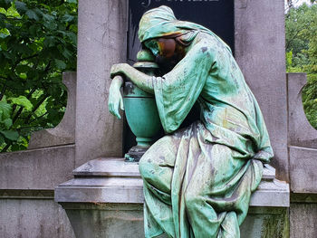 Statue of man sitting by plants