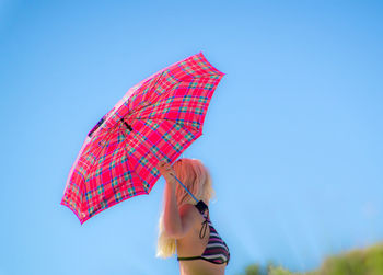Side view of woman holding umbrella while standing against clear blue sky