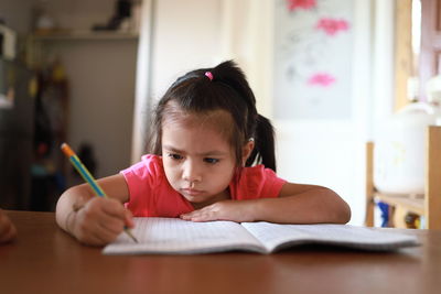 Portrait of girl wearing eyeglasses on table at home