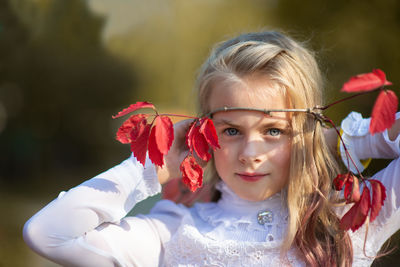 Portrait of cute girl holding twig with red leaves during autumn