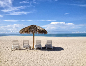 Lounge chairs amidst thatched roof on sandy beach