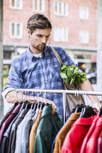 Young man with groceries selecting jackets in clothing store