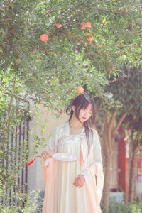 Portrait of young woman standing against trees