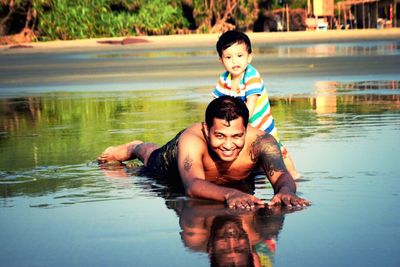 Portrait of happy shirtless father enjoying with son at beach