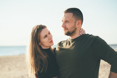 Young couple standing at beach against sky