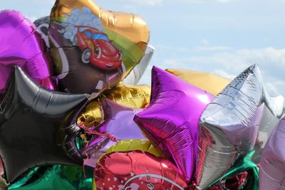 Close-up of woman holding multi colored umbrellas against sky