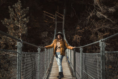 Front view of young woman standing on hanging footbridge in autumn