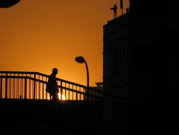 Silhouette man standing by railing against sunset sky