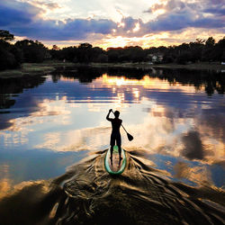 Silhouette man paddleboarding in lake against sky during sunset