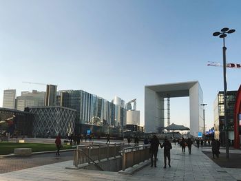 People on street amidst buildings against clear sky