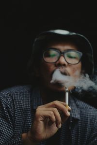 Low angle view of young man smoking cigarette against black background