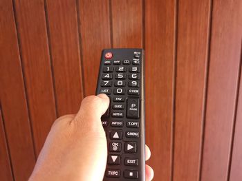 Cropped hand of man holding remote control against wall