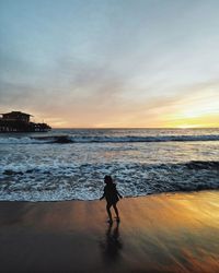 Silhouette man walking on beach against sky during sunset