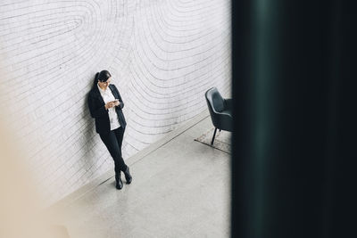 High angle view of woman using mobile phone while leaning on wall at office