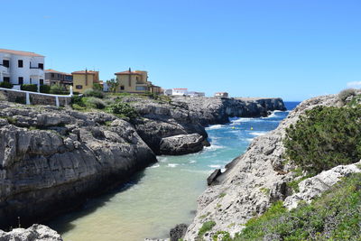 Rocks by sea against clear blue sky