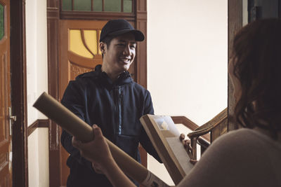 Smiling delivery man delivering package while talking to customer at doorstep