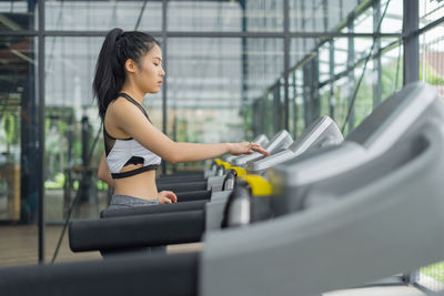 Side view of young woman running on treadmill at gym