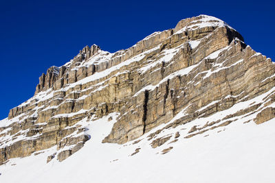 Low angle view of snowcapped mountains against clear blue sky