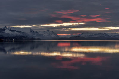 Scenic view of lake by snowcapped mountains against sky during sunset