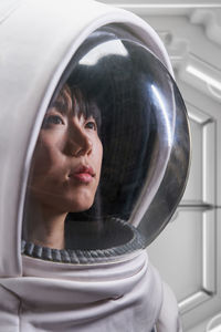 Asian woman in astronaut costume and helmet looking away during space mission in spaceship