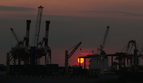 Silhouette cranes at construction site against sky during sunset