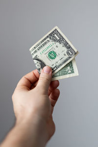 Cropped hand holding paper currency against gray background