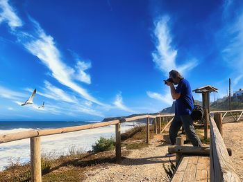 Man standing on railing against blue sky