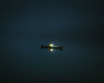 Man with flashlight sitting in boat in lake against sky at night
