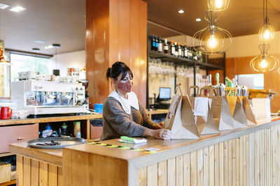 Female manager arranging brown paper bags on bar counter during covid-19