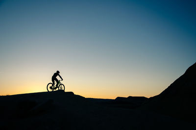 Silhouette person riding bicycle on mountain against clear sky