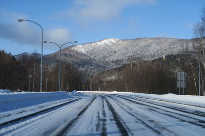 Snow covered road by mountain against sky