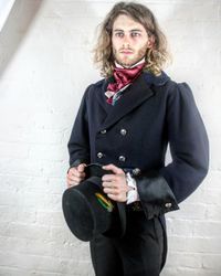 Young man wearing traditional clothing while standing against white wall