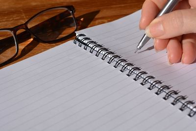 Close-up of woman writing on blank spiral notebook