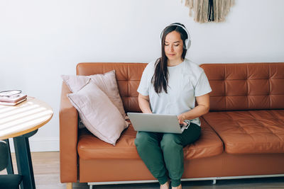 Young brunette female freelancer in headphones works from home on a laptop.