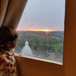 Boy looking through window at sunset