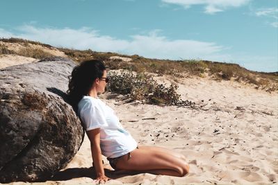 Rear view of woman sitting on rock at beach against sky