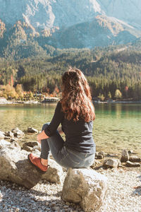 Rear view of woman sitting on rock at lake