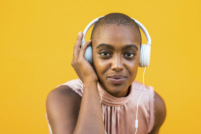 Portrait of woman wearing headphones against yellow background