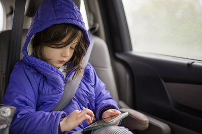 A small child travels in a car looking at a cell phone screen on trip