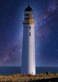 Lighthouse by sea against sky at night