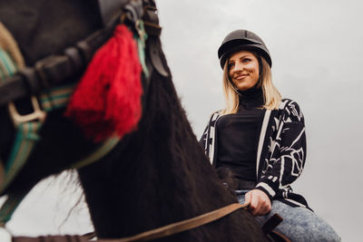 Woman looking away while sitting on horse against sky