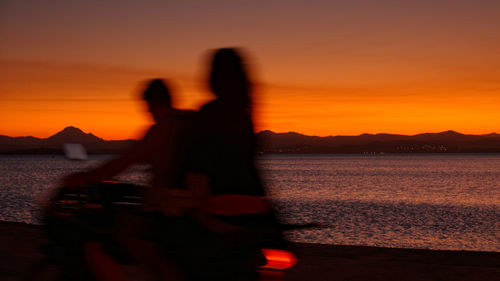 Silhouette people standing by sea against orange sky